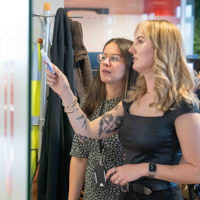 Two female colleagues brainstorming solutions on a whiteboard together during our global innovation day.