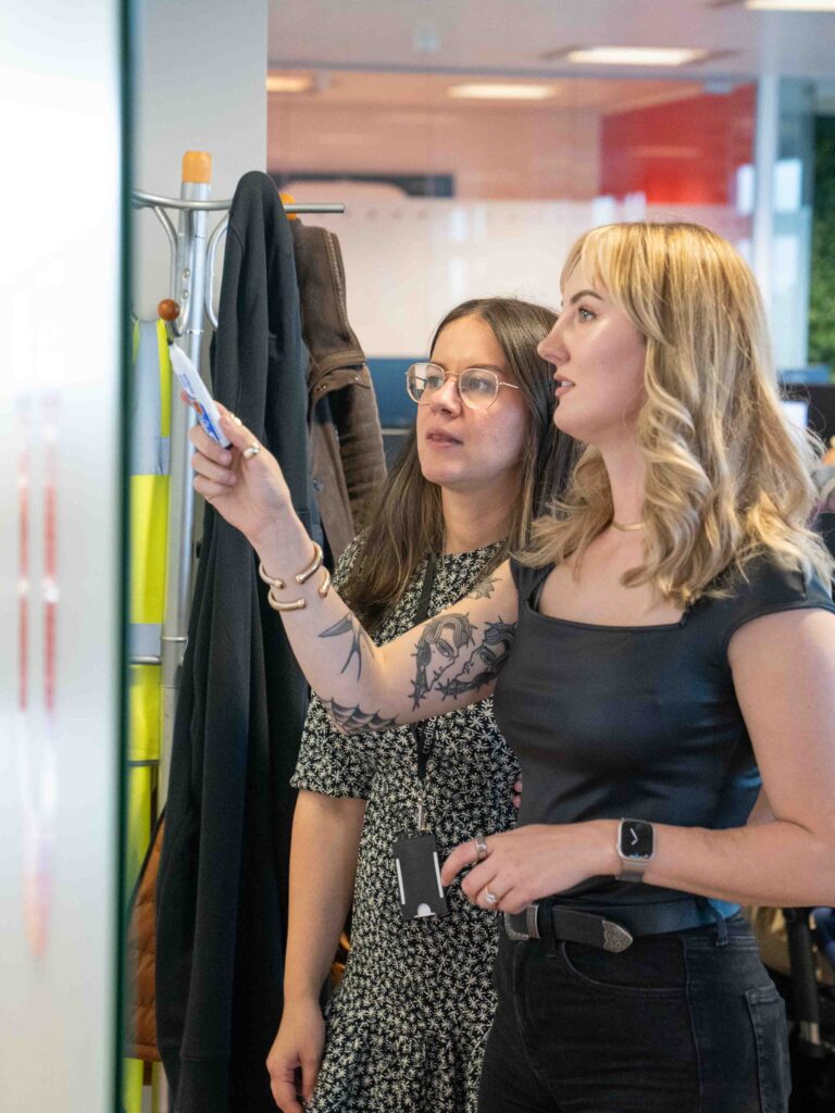 Two female colleagues brainstorming solutions on a whiteboard together during our global innovation day.